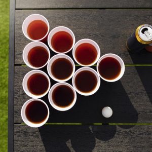 Postavitev igre Beer Pong na vrtni mizi, prikaz lončkov napolnjenih s pijačo in igralno žogico.