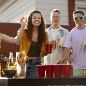 Mladi uživajo v igranju Beer Ponga na zabavi, z rdečimi lončki in žogico v akciji.
