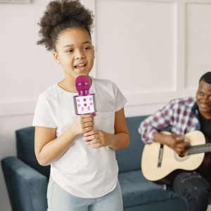 Mlado dekle uživa v petju s pomočjo roza karaoke mikrofona, popolnoma za družinske zabave.