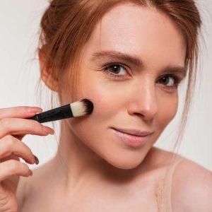 Slika prikazuje uporabo čopiča za rdečilo na licih modela, kar prikazuje tehniko in učinkovitost čopiča.